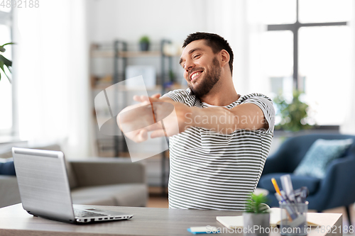Image of happy man with laptop stretching at home office