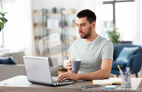 Image of man with laptop drinking coffee at home office