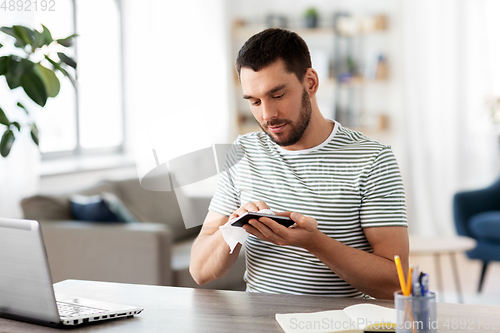 Image of man cleaning phone with wet wipe at home office