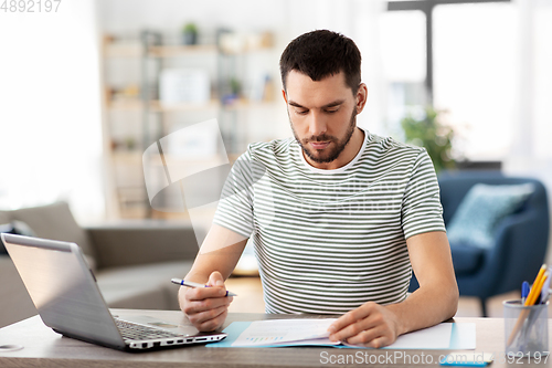 Image of man with papers and laptop working at home office