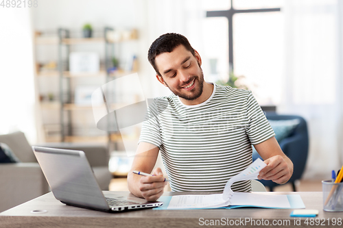 Image of man with papers and laptop working at home office