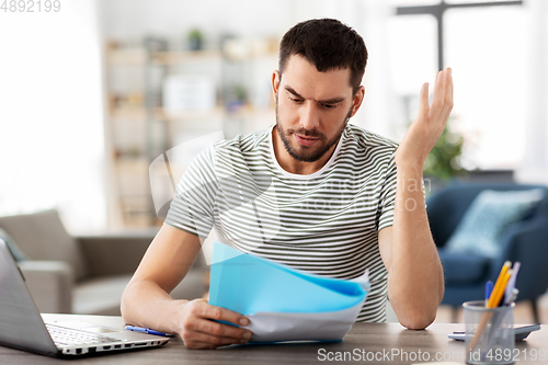 Image of man with papers and laptop working at home office