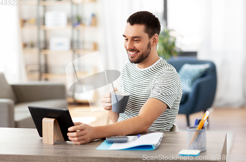 Image of man with tablet pc drinking coffee at home office