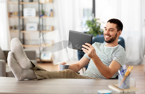 Image of man with tablet pc resting feet on table at home