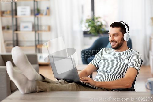 Image of happy man with laptop and headphones at home