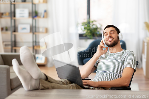 Image of happy man with laptop and headphones at home