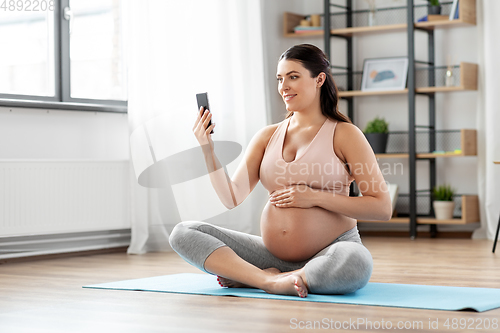 Image of happy pregnant woman with phone doing yoga at home
