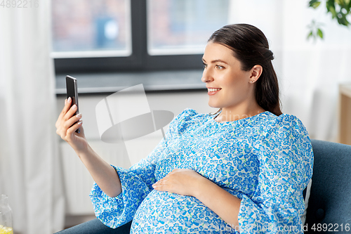 Image of happy pregnant woman with smartphone at home