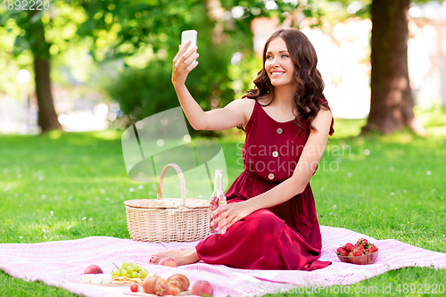 Image of happy woman with smartphone taking selfie at park