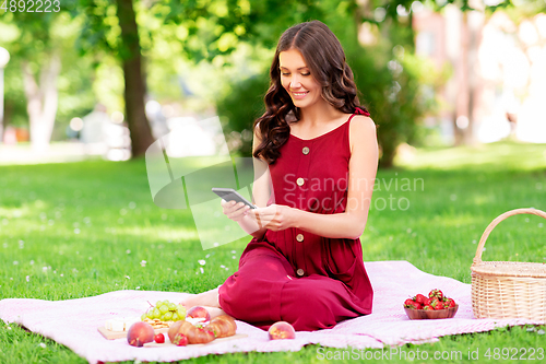 Image of happy woman with smartphone on picnic at park