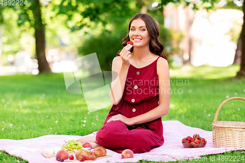 Image of happy woman eating strawberry on picnic at park