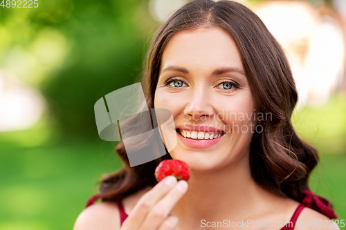 Image of happy woman eating strawberry at summer park