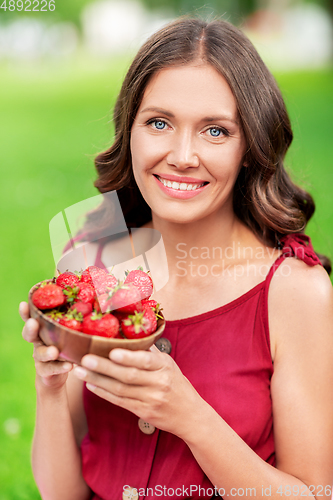 Image of happy woman eating strawberry at summer park