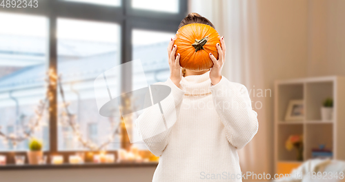 Image of woman holding pumpkin and covering her face