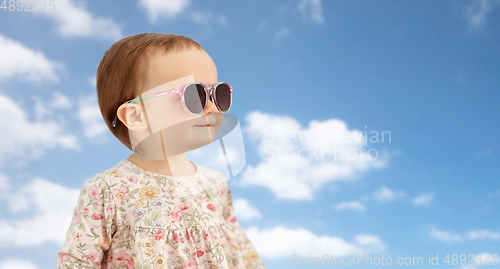 Image of happy little baby girl in sunglasses over blue sky