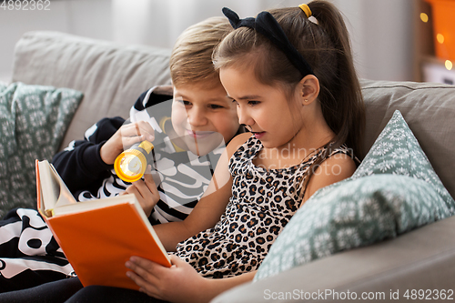 Image of kids in halloween costumes reading book at home