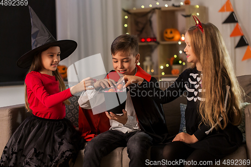 Image of kids in halloween costumes sharing candies at home