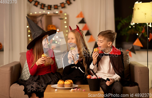 Image of kids in halloween costumes eating cupcakes at home