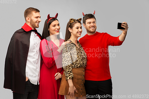 Image of happy friends in halloween costumes taking selfie