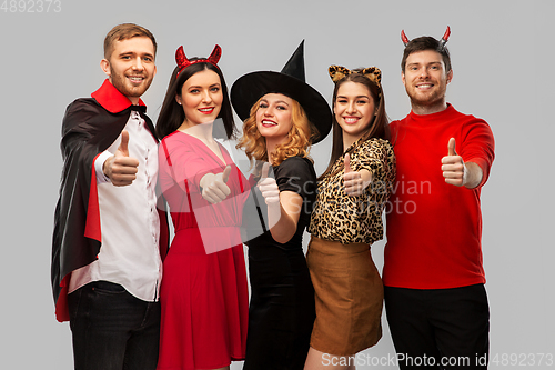 Image of happy friends in halloween costumes snow thumbs up
