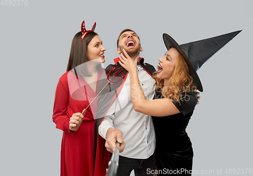 Image of happy friends in halloween costumes taking selfie