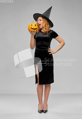 Image of woman in halloween costume of witch biting pumpkin