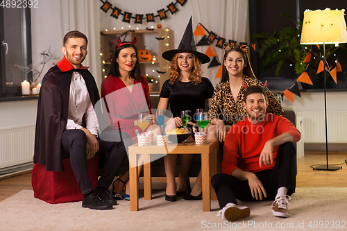 Image of happy friends in halloween costumes at home party