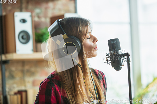 Image of Woman in headphones recording music, singing or making broadcast internet tutorial while sitting in loft workplace or at home