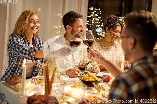 Image of happy friends drinking red wine at christmas party