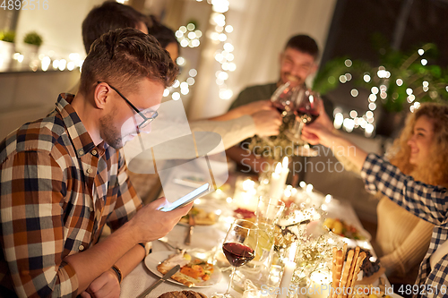 Image of man with smartphone at dinner party with friends