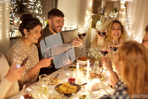 Image of happy friends drinking red wine at christmas party