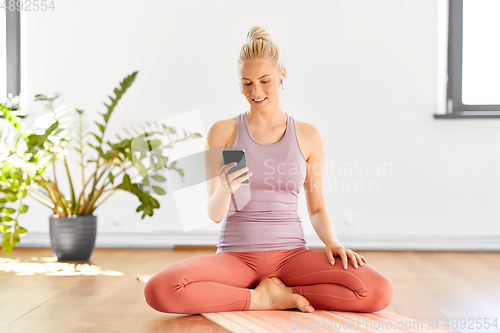 Image of woman with phone and earphones doing yoga at home