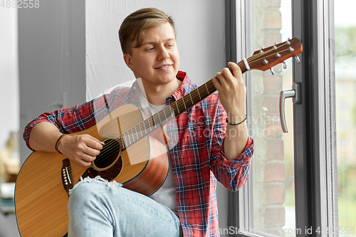 Image of young man playing guitar sitting on windowsill