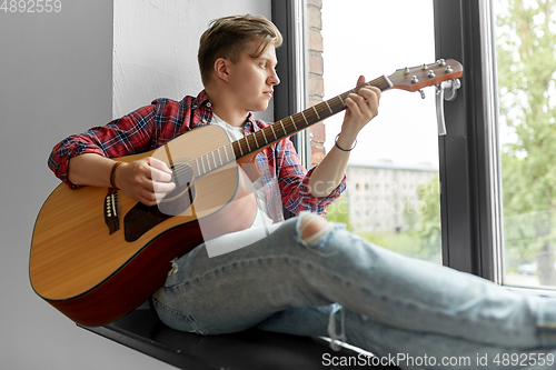 Image of young man playing guitar sitting on windowsill