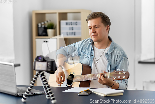 Image of man or blogger with camera playing guitar at home