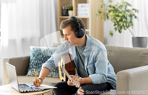 Image of man in headphones with guitar, notes and laptop