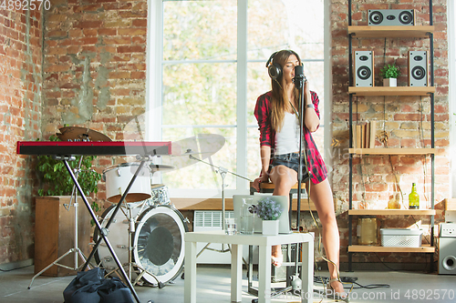 Image of Woman in headphones recording music, singing or making broadcast internet tutorial while sitting in loft workplace or at home