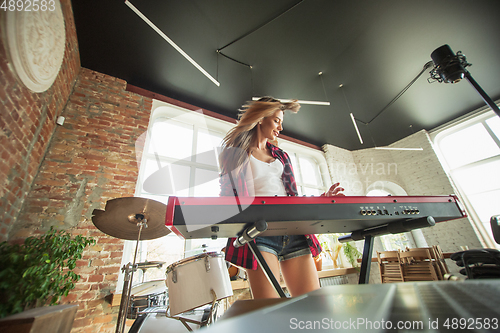 Image of Woman recording music, singing and playing piano while standing in loft workplace or at home