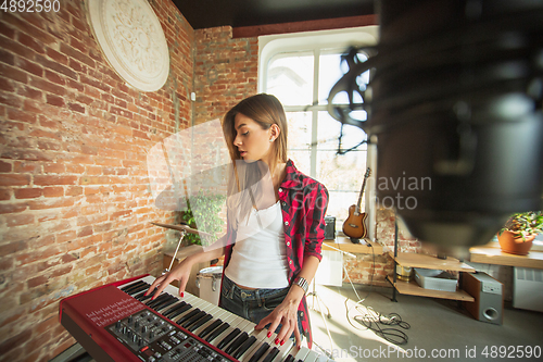 Image of Woman recording music, singing and playing piano while standing in loft workplace or at home