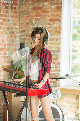 Image of Woman recording music, singing and playing piano while standing in loft workplace or at home