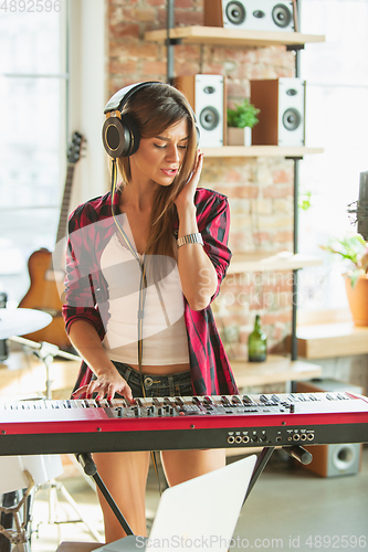 Image of Woman recording music, singing and playing piano while standing in loft workplace or at home