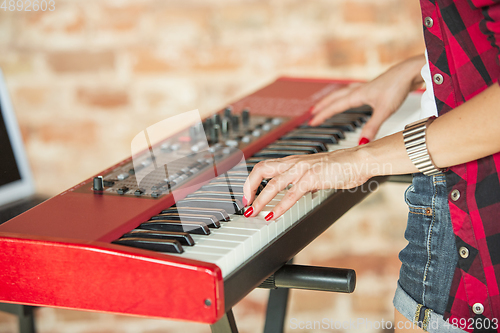 Image of Woman recording music, singing and playing piano while standing in loft workplace or at home