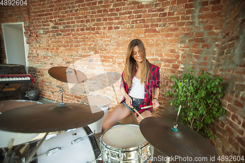 Image of Woman recording music, singing and playing drums while sitting in loft workplace or at home