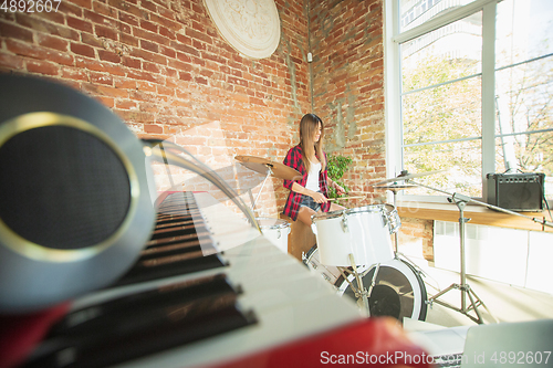 Image of Woman recording music, singing and playing drums while sitting in loft workplace or at home