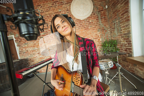 Image of Woman in headphones recording music, singing or making broadcast internet tutorial while sitting in loft workplace or at home