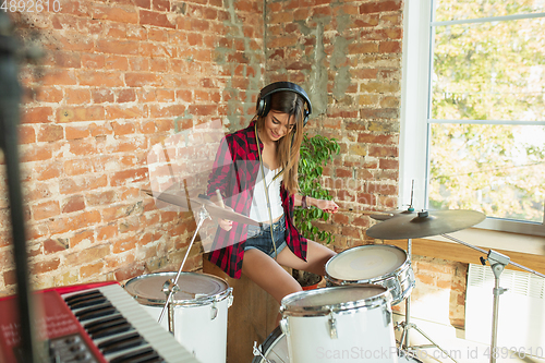 Image of Woman recording music, singing and playing drums while sitting in loft workplace or at home