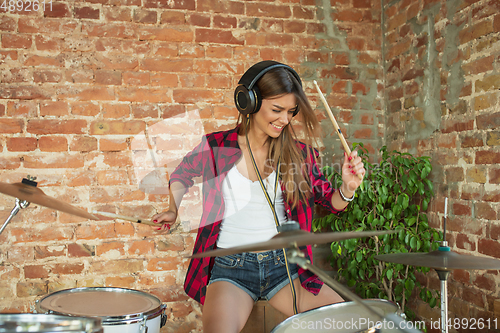 Image of Woman recording music, singing and playing drums while sitting in loft workplace or at home