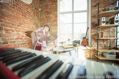 Image of Woman recording music, singing and playing drums while sitting in loft workplace or at home