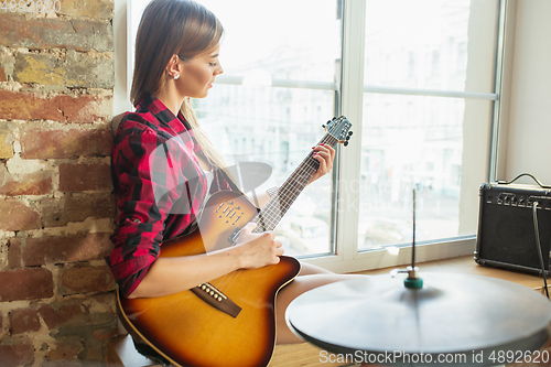 Image of Woman recording music, singing and playing guitar while sitting in loft workplace or at home