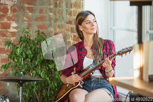 Image of Woman recording music, singing and playing guitar while sitting in loft workplace or at home